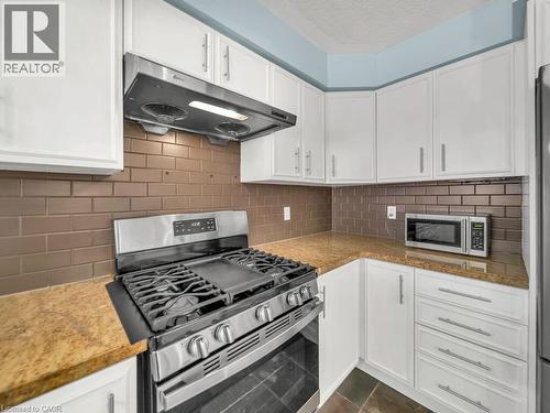 Kitchen with appliances with stainless steel finishes, white cabinets, under cabinet range hood, decorative backsplash, and a textured ceiling - 29 Amsterdam Crescent, Guelph, ON - Indoor Photo Showing Kitchen