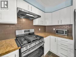 Kitchen with appliances with stainless steel finishes, white cabinets, under cabinet range hood, decorative backsplash, and a textured ceiling - 