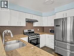 Kitchen with appliances with stainless steel finishes, white cabinets, tasteful backsplash, under cabinet range hood, and a textured ceiling - 
