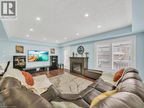 Living area featuring a raised ceiling, a glass covered fireplace, wood finished floors, a textured ceiling, and recessed lighting - 29 Amsterdam Crescent, Guelph, ON - Indoor Photo Showing Living Room With Fireplace
