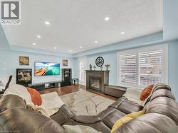 Living area featuring a raised ceiling, a glass covered fireplace, wood finished floors, a textured ceiling, and recessed lighting - 