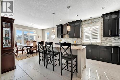 Kitchen with a kitchen breakfast bar, decorative light fixtures, light stone countertops, a center island, and a textured ceiling - 107 Forbes Crescent, Listowel, ON - Indoor