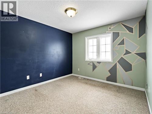 Carpeted spare room with an accent wall and a textured ceiling - 47 Schroder Crescent, Guelph, ON - Indoor Photo Showing Other Room