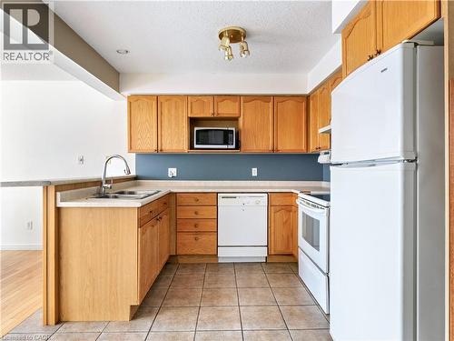 Kitchen with white appliances, light countertops, a peninsula, light tile patterned flooring, and a textured ceiling - 47 Schroder Crescent, Guelph, ON - Indoor Photo Showing Kitchen With Double Sink