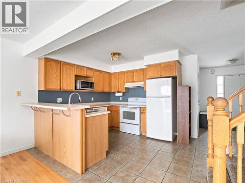 Kitchen featuring white appliances, light countertops, a textured ceiling, a peninsula, and a kitchen bar - 47 Schroder Crescent, Guelph, ON - Indoor Photo Showing Kitchen