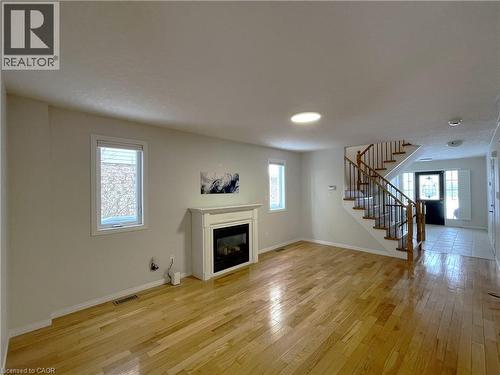 Unfurnished living room featuring light wood-style floors, a glass covered fireplace, and stairs - 443 Lausanne Crescent, Waterloo, ON - Indoor Photo Showing Living Room With Fireplace