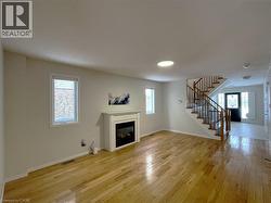 Unfurnished living room featuring light wood-style floors, a glass covered fireplace, and stairs - 