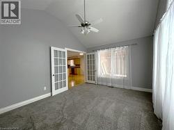 Carpeted spare room featuring french doors, high vaulted ceiling, and a ceiling fan - 