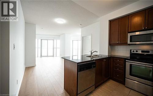 Kitchen with appliances with stainless steel finishes, a peninsula, dark brown cabinetry, decorative backsplash, and open floor plan - 50 Absolute Avenue Unit# 2105, Mississauga, ON - Indoor Photo Showing Kitchen With Double Sink