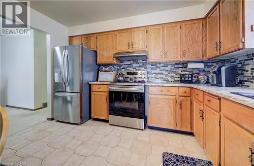 Kitchen featuring stainless steel appliances, under cabinet range hood, brown cabinetry, light stone counters, and backsplash - 42 Ruffian Road, Brantford, ON - Indoor Photo Showing Kitchen