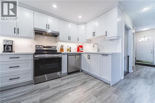 Kitchen featuring stainless steel appliances, under cabinet range hood, light wood finished floors, a textured ceiling, and white cabinetry - 143 Fairfield Avenue, Hamilton, ON - Indoor Photo Showing Kitchen