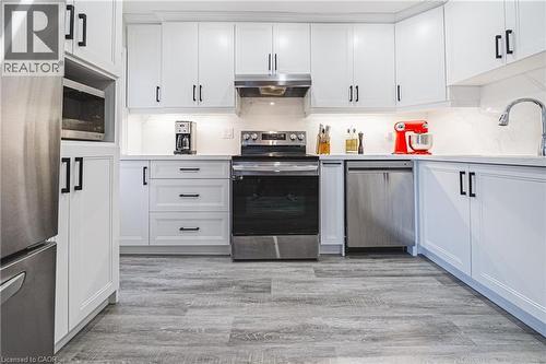 Kitchen featuring appliances with stainless steel finishes, white cabinetry, light wood-style floors, under cabinet range hood, and decorative backsplash - 143 Fairfield Avenue, Hamilton, ON - Indoor Photo Showing Kitchen