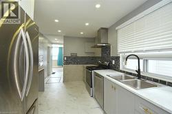 Kitchen featuring stainless steel appliances, wall chimney exhaust hood, recessed lighting, decorative backsplash, and light marble finish floors - 
