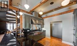 Kitchen with dark stone counters, wall chimney exhaust hood, stainless steel gas stovetop, light wood-style floors, and gray cabinetry - 