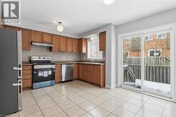 Kitchen with stainless steel appliances, brown cabinets, backsplash, under cabinet range hood, and light tile patterned flooring - 