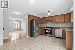 Kitchen with appliances with stainless steel finishes, light tile patterned floors, brown cabinetry, under cabinet range hood, and backsplash - 