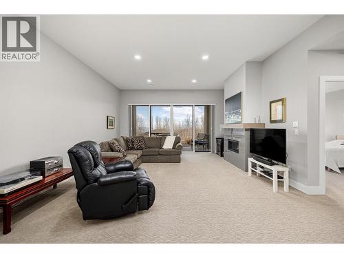 Lake views from the lower level! Spacious recreation space with tall ceilings featuring a gas fireplace with tile surround all opening to a covered patio - 468 Sparrow Hawk Court, Kelowna, BC - Indoor Photo Showing Living Room