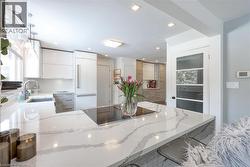 Kitchen featuring a peninsula, light stone counters, modern cabinets, black electric cooktop, and recessed lighting - 