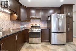 Kitchen featuring dark brown cabinets, stainless steel appliances, dark countertops, under cabinet range hood, and decorative backsplash - 