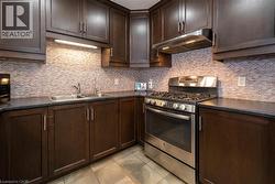 Kitchen with stainless steel gas range, dark countertops, dark brown cabinets, under cabinet range hood, and backsplash - 