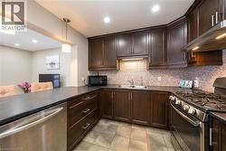 Kitchen with appliances with stainless steel finishes, dark brown cabinets, dark countertops, wall chimney range hood, and hanging light fixtures - 