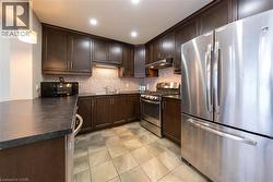 Kitchen featuring stainless steel appliances, dark brown cabinetry, dark countertops, hanging light fixtures, and under cabinet range hood - 