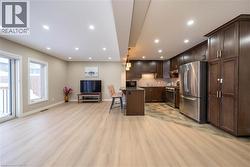 Kitchen featuring open floor plan, decorative light fixtures, dark brown cabinetry, a kitchen bar, and appliances with stainless steel finishes - 