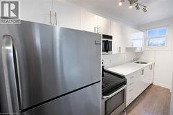 Kitchen featuring appliances with stainless steel finishes, white cabinets, dark wood-type flooring, light stone countertops, and backsplash - 