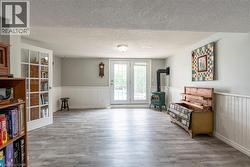 Living area featuring a textured ceiling, a wood stove, a wainscoted wall, and wood finished floors - 