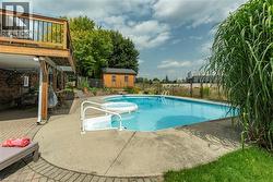 View of swimming pool featuring a patio area, a wooden deck, a shed, and a diving board - 