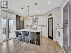 Kitchen with high end refrigerator, hanging light fixtures, white cabinetry, an island with sink, and recessed lighting - 