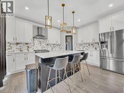 Kitchen with high quality fridge, white cabinetry, decorative light fixtures, an island with sink, and recessed lighting - 