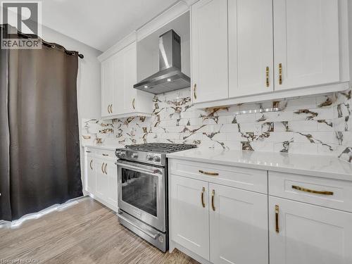 Kitchen featuring white cabinetry, wall chimney exhaust hood, gas range, light stone counters, and light wood-style floors - 3374 Oriole Drive, London, ON - Indoor Photo Showing Kitchen