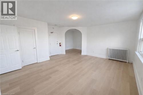 Empty room with arched walkways, radiator heating unit, and light wood finished floors - 17 Louisa Street, Kitchener, ON - Indoor Photo Showing Other Room