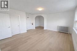 Empty room with arched walkways, radiator heating unit, and light wood finished floors - 