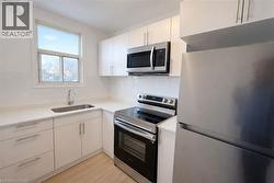 Kitchen with appliances with stainless steel finishes, white cabinets, light wood-style floors, decorative backsplash, and light stone countertops - 