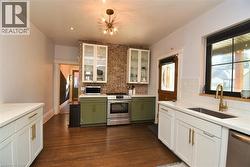 Kitchen with white cabinetry, green cabinetry, appliances with stainless steel finishes, dark wood finished floors, and light stone counters - 