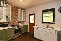 Kitchen featuring green cabinets, white cabinetry, stainless steel appliances, backsplash, and dark wood finished floors - 