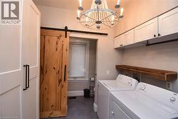Laundry area featuring a barn door, cabinet space, washing machine and dryer, and a chandelier - 