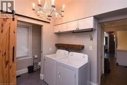 Laundry area featuring a barn door, washing machine and clothes dryer, cabinet space, and a chandelier - 