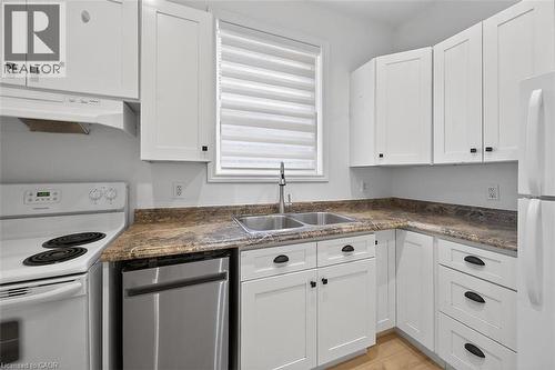 Kitchen featuring white appliances, dark countertops, white cabinetry, and under cabinet range hood - 77 Barton Street E Unit# 1, Hamilton, ON - Indoor Photo Showing Kitchen With Double Sink