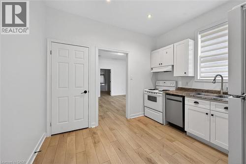 Kitchen featuring white cabinets, white appliances, light wood-type flooring, dark stone counters, and under cabinet range hood - 77 Barton Street E Unit# 1, Hamilton, ON - Indoor Photo Showing Kitchen