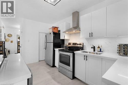 Kitchen with electric range, white cabinets, wall chimney exhaust hood, light wood-style floors, and light stone counters - 133 Frederick Avenue, Hamilton, ON - Indoor Photo Showing Kitchen