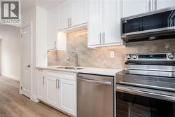 Kitchen with appliances with stainless steel finishes, white cabinetry, light stone countertops, and light wood finished floors - 