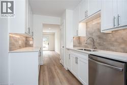 Kitchen featuring white cabinetry, dishwasher, light stone countertops, and light wood-type flooring - 