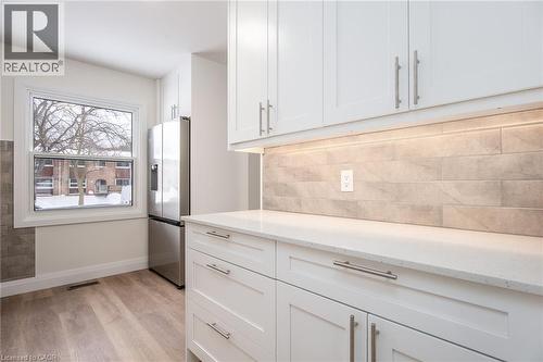 Kitchen with white cabinets, stainless steel fridge, light wood finished floors, light stone counters, and backsplash - 27 Queenston Drive, Kitchener, ON - Indoor Photo Showing Kitchen