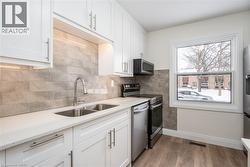 Kitchen featuring white cabinetry, appliances with stainless steel finishes, light stone counters, light wood-type flooring, and tasteful backsplash - 