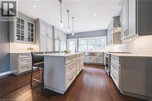Kitchen with decorative backsplash, a breakfast bar, hanging light fixtures, light stone countertops, and glass insert cabinets - 25 Orchard Hill, Hamilton, ON - Indoor Photo Showing Kitchen With Upgraded Kitchen
