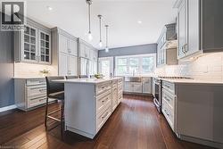 Kitchen with decorative backsplash, a breakfast bar, hanging light fixtures, light stone countertops, and glass insert cabinets - 