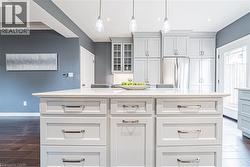 Kitchen with a kitchen island, stainless steel refrigerator, white cabinets, glass insert cabinets, and hanging light fixtures - 